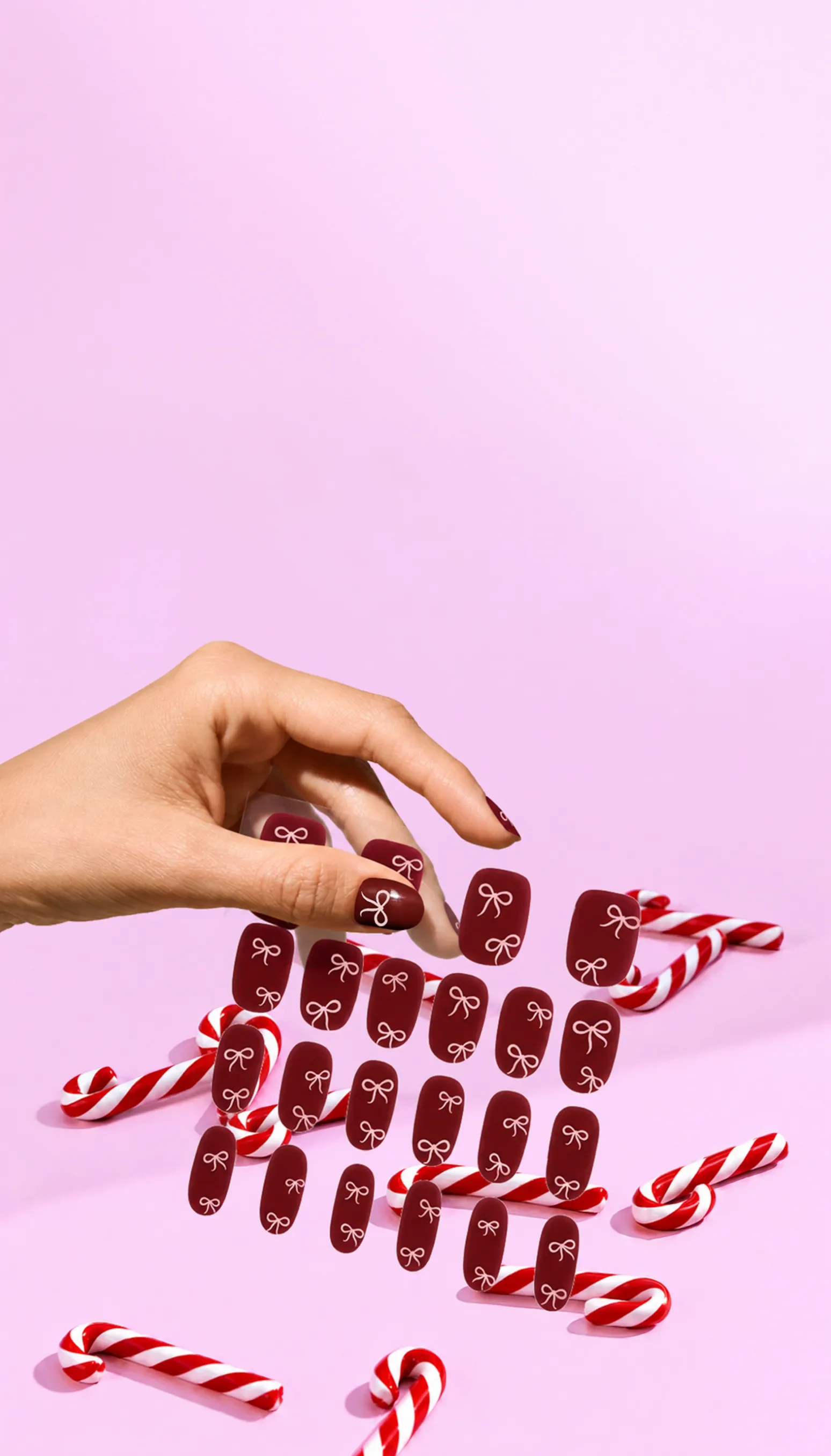 A hand picking up deep red festive bow stick-on gels surrounded by candy canes