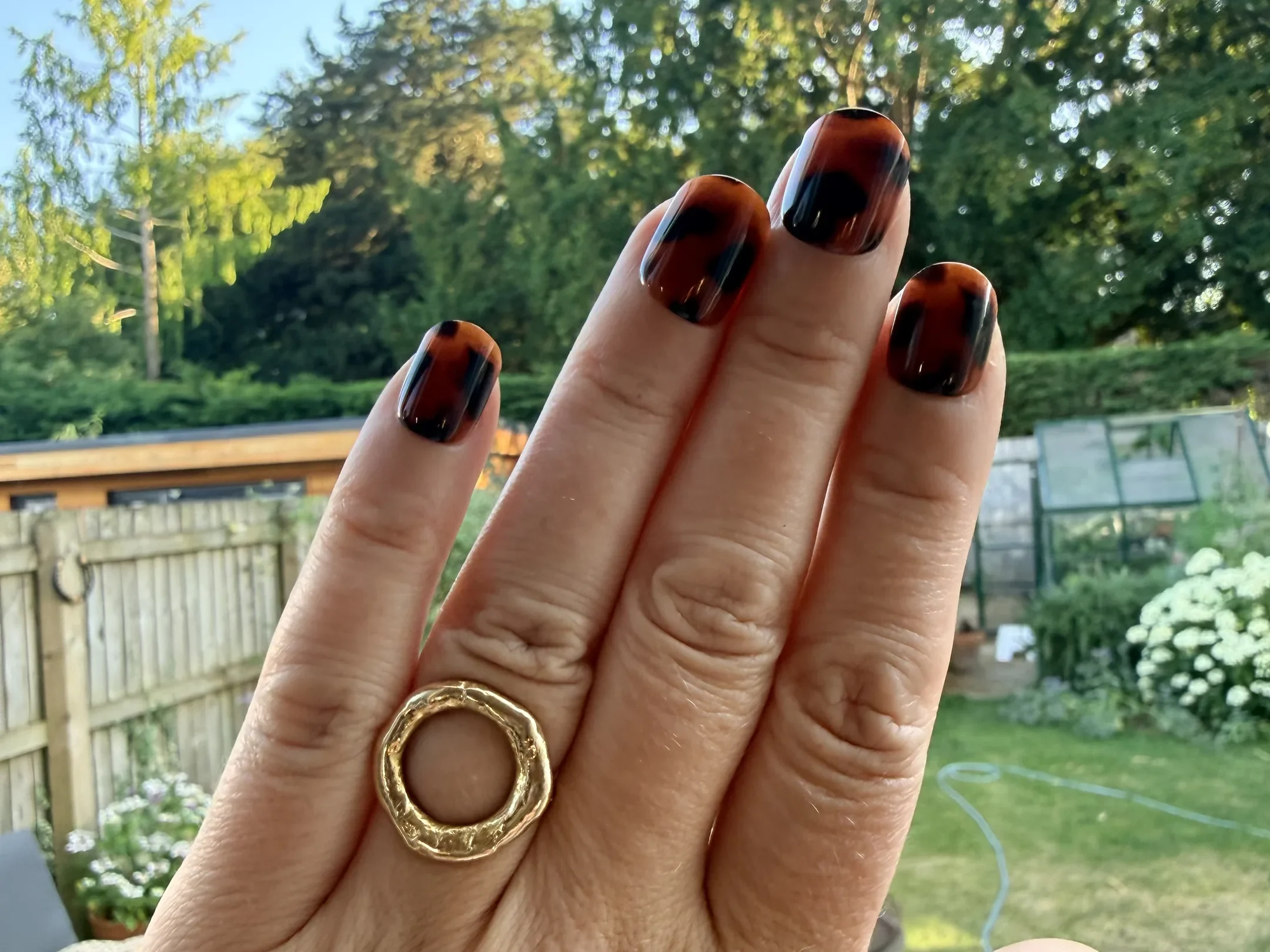 A hand wearing Tortoise Shell Glaize Tips press-on nails in a garden