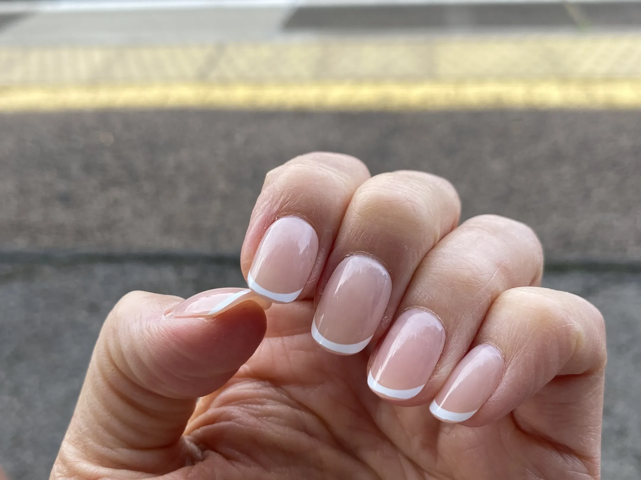A hand wearing white French tip Glaize Tips press-on nails