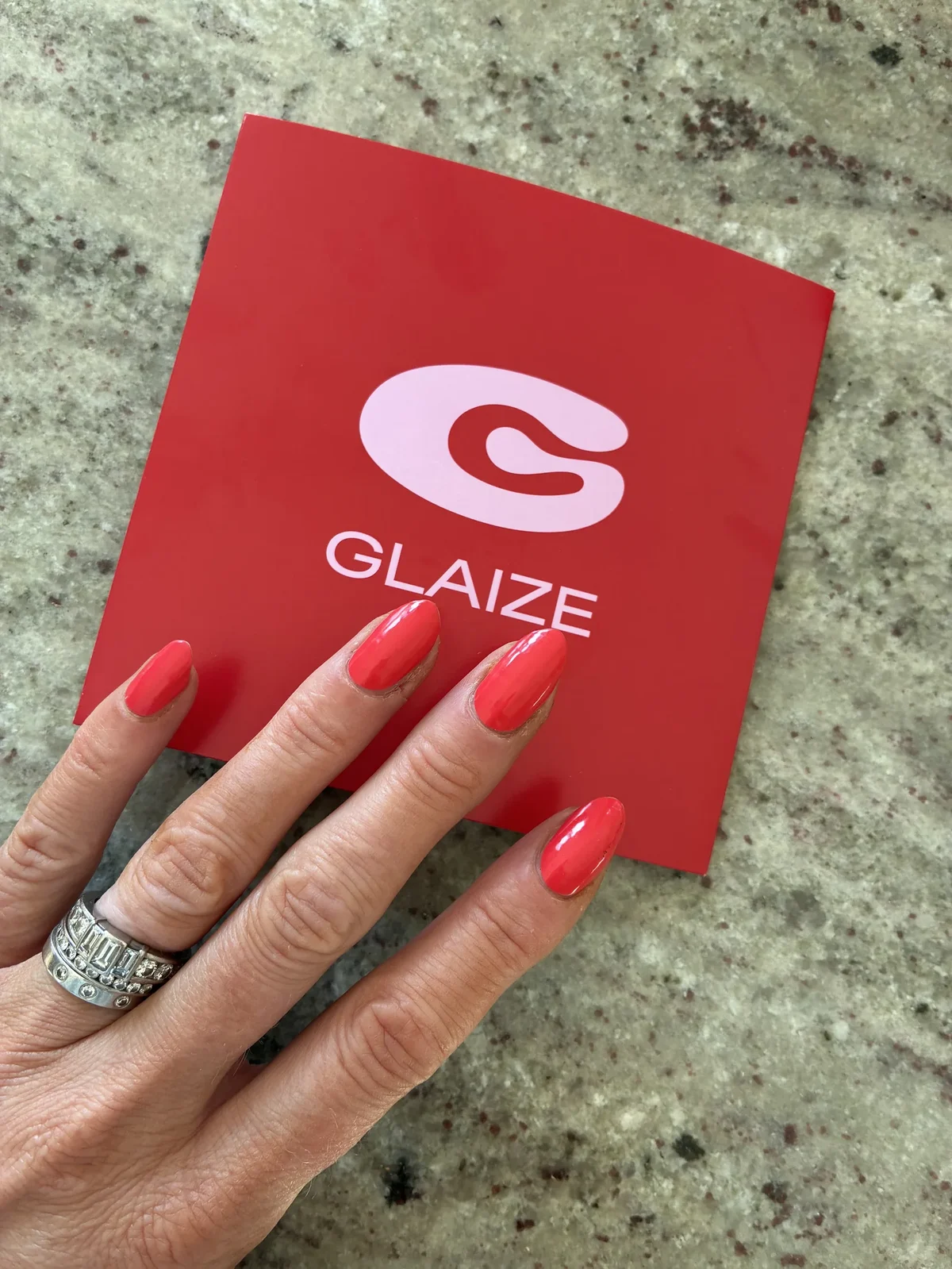 Glossy red Glaize stick-on gel manicure beside Glaize packaging