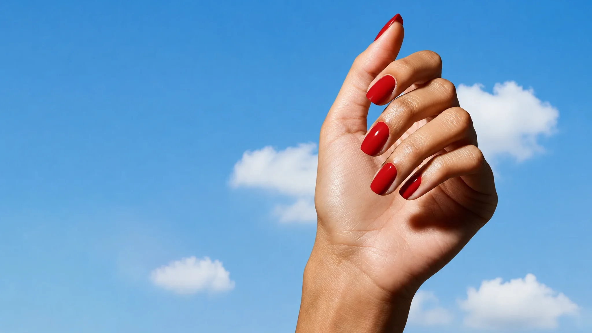 A hand with a Glaize stick-on gel manicure in deep red against a blue sky background