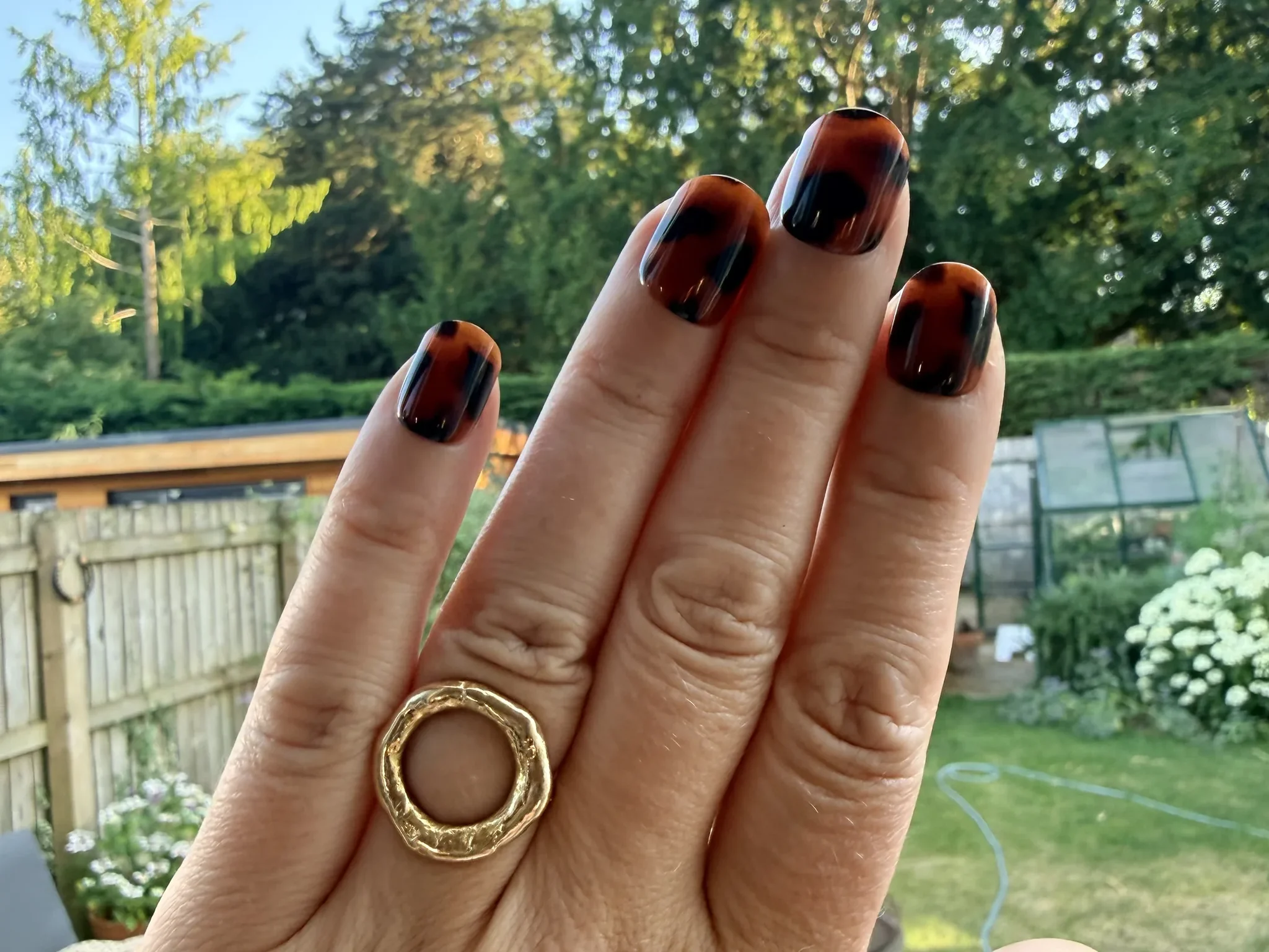 A hand wearing Tortoise Shell Glaize Tips press-on nails in a garden