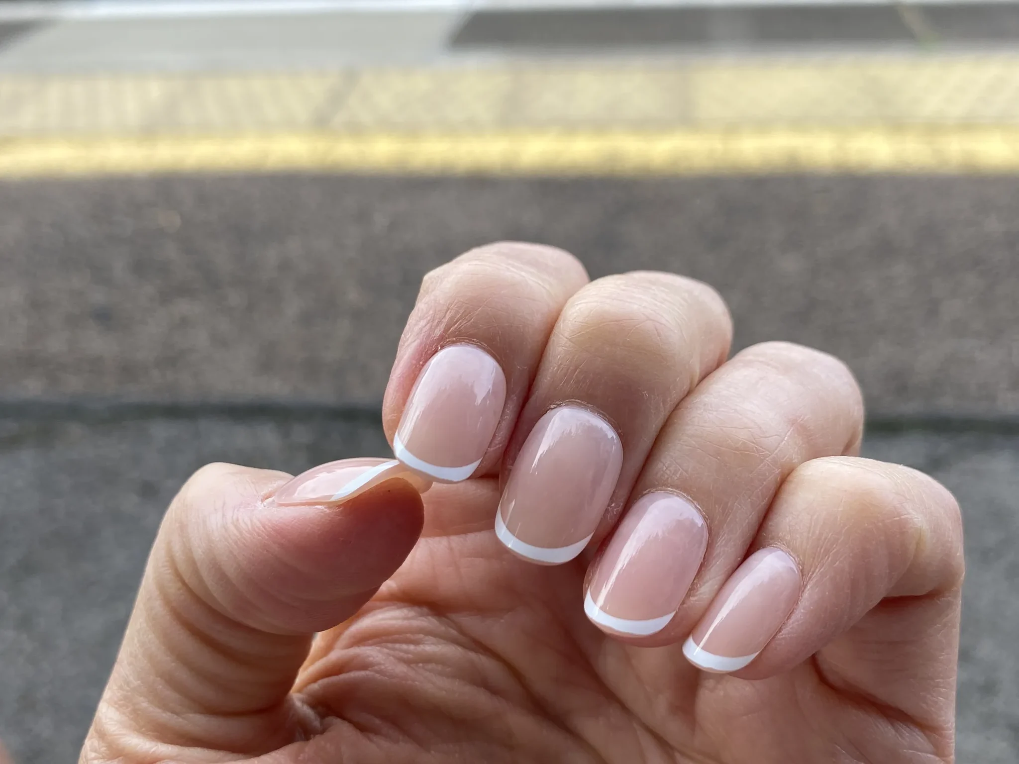 A hand wearing white French tip Glaize Tips press-on nails